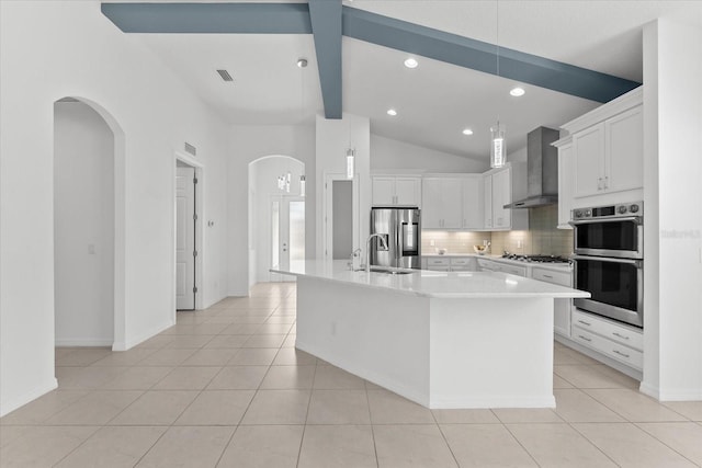 kitchen featuring a kitchen island with sink, white cabinetry, light countertops, wall chimney range hood, and appliances with stainless steel finishes