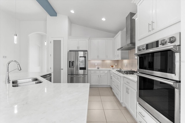 kitchen with wall chimney exhaust hood, appliances with stainless steel finishes, white cabinetry, pendant lighting, and a sink