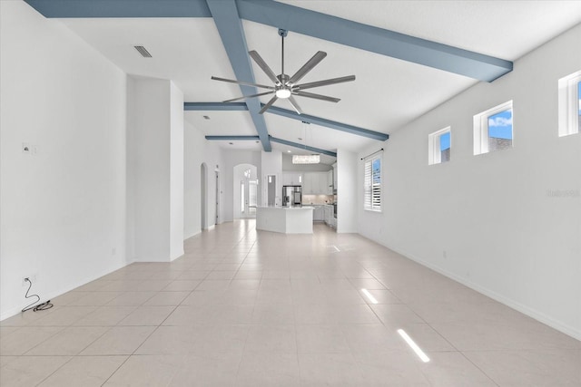 unfurnished living room featuring arched walkways, light tile patterned floors, lofted ceiling with beams, a ceiling fan, and baseboards