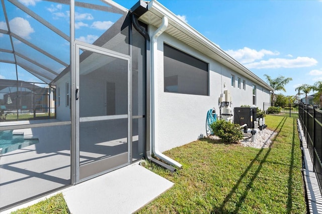 view of side of home featuring glass enclosure, a yard, a patio, and stucco siding