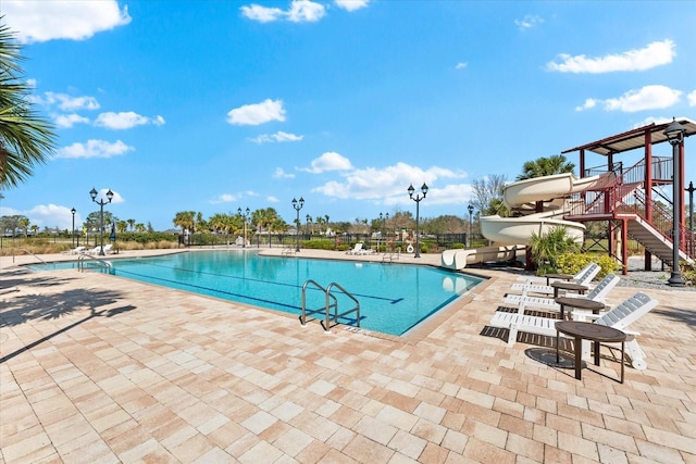 community pool featuring stairs, a water slide, and a patio