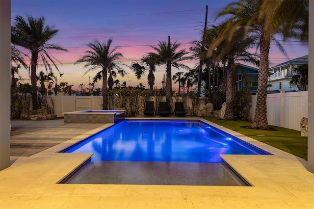 pool at dusk featuring a patio area, a fenced backyard, and a pool with connected hot tub