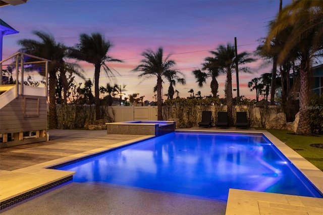 pool at dusk with a patio area, a pool with connected hot tub, and a fenced backyard