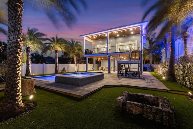 back of house at dusk with a fenced in pool, a ceiling fan, a fenced backyard, an in ground hot tub, and a deck