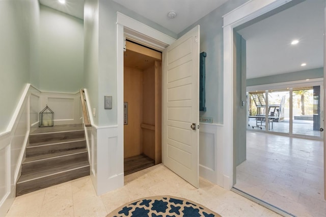 stairs featuring a wainscoted wall, a decorative wall, elevator, and recessed lighting