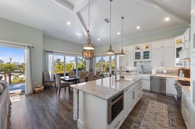 kitchen with a center island with sink, decorative backsplash, beam ceiling, stainless steel appliances, and a sink