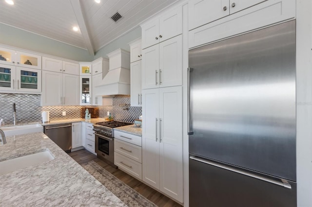 kitchen with tasteful backsplash, white cabinets, high end appliances, custom range hood, and a sink