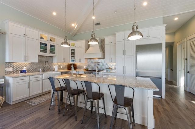 kitchen with built in refrigerator, white cabinetry, custom exhaust hood, and a sink