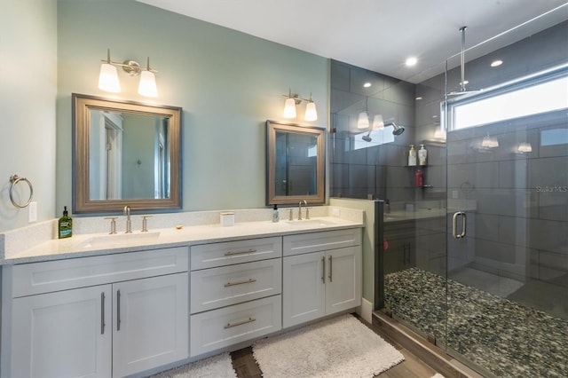 bathroom featuring a stall shower, wood finished floors, a sink, and double vanity