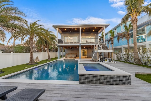 rear view of property with a fenced in pool, a fenced backyard, ceiling fan, an in ground hot tub, and a wooden deck