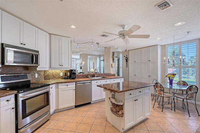 kitchen with a sink, white cabinetry, appliances with stainless steel finishes, light tile patterned floors, and decorative backsplash