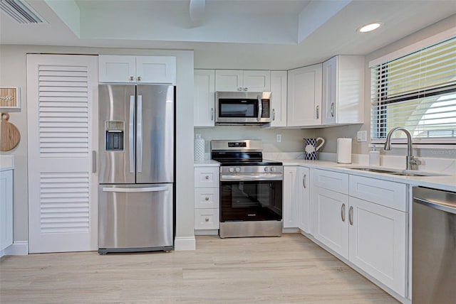 kitchen featuring light wood-style flooring, a sink, white cabinetry, light countertops, and appliances with stainless steel finishes