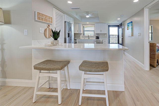 kitchen featuring a breakfast bar, light countertops, appliances with stainless steel finishes, white cabinets, and a peninsula