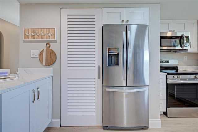 kitchen with light stone counters, arched walkways, light wood finished floors, appliances with stainless steel finishes, and white cabinetry