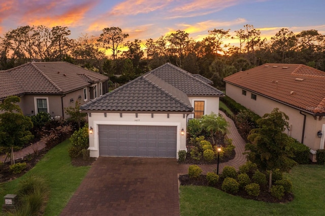 mediterranean / spanish-style home featuring decorative driveway, a tile roof, a yard, stucco siding, and an attached garage