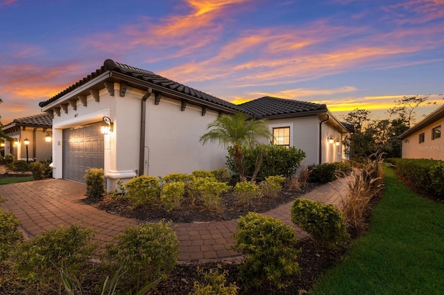 view of side of property featuring a garage, decorative driveway, a tile roof, and stucco siding