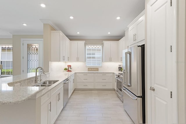 kitchen with a peninsula, a sink, high quality appliances, white cabinets, and backsplash