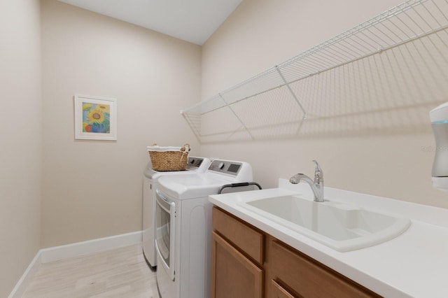 laundry area with laundry area, a sink, light wood-style floors, baseboards, and washing machine and clothes dryer