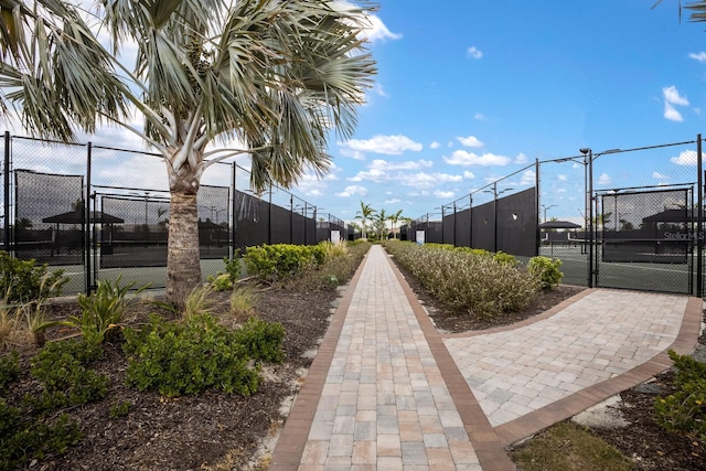 view of property's community featuring a tennis court, a gate, and fence