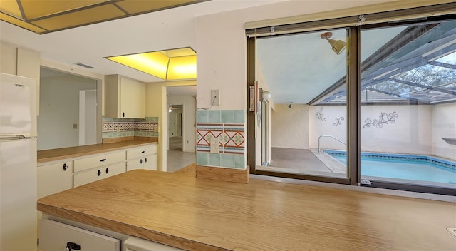 kitchen with tasteful backsplash, freestanding refrigerator, white cabinets, and light countertops