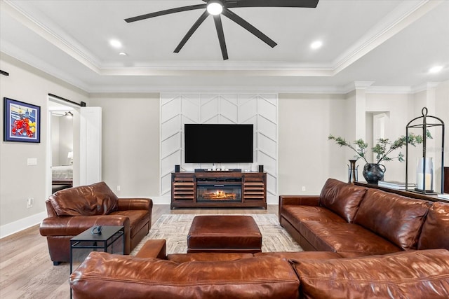 living room with a ceiling fan, a tray ceiling, crown molding, and wood finished floors