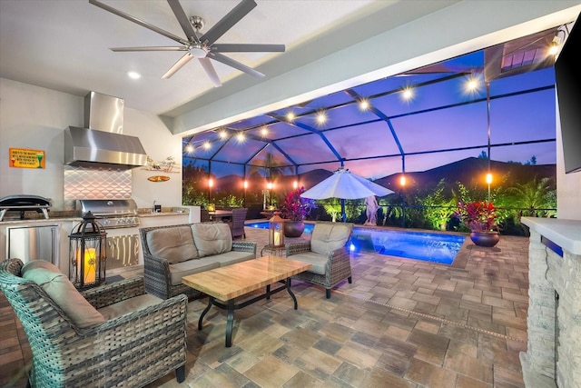 patio at night featuring area for grilling, glass enclosure, an outdoor kitchen, and an outdoor living space