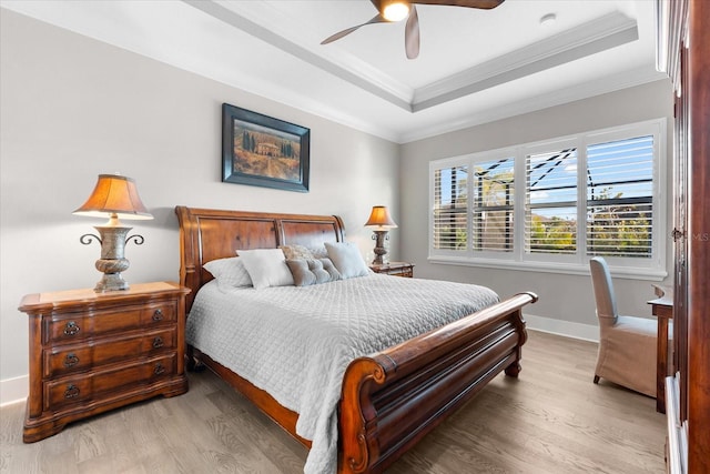 bedroom featuring a raised ceiling, crown molding, baseboards, and wood finished floors