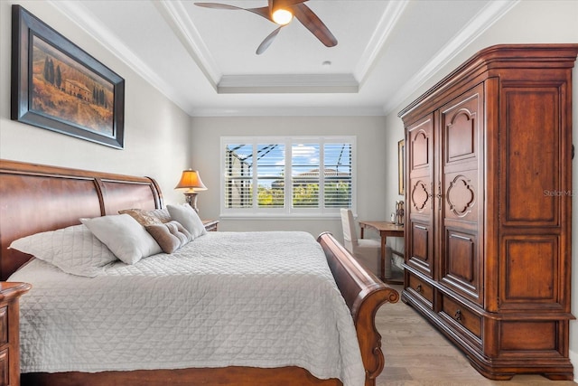 bedroom with light wood-type flooring, a tray ceiling, a ceiling fan, and ornamental molding