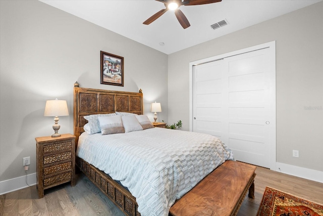 bedroom with ceiling fan, wood finished floors, visible vents, baseboards, and a closet