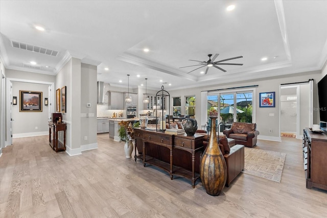 living room featuring a barn door, a raised ceiling, visible vents, and light wood-style floors