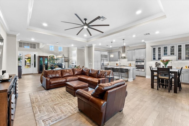 living room with light wood finished floors, a tray ceiling, and visible vents