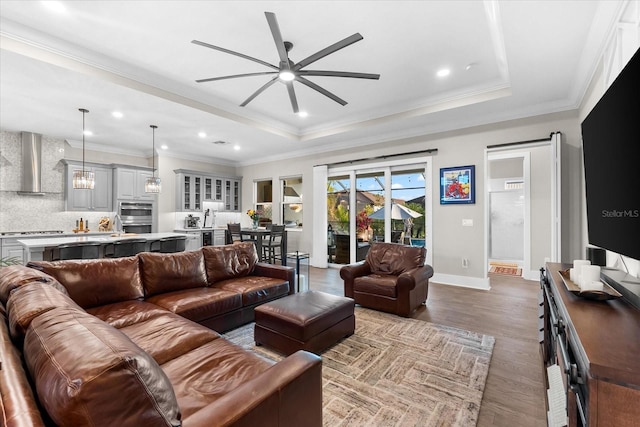 living area with a tray ceiling, recessed lighting, ornamental molding, wood finished floors, and baseboards