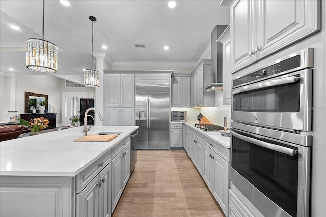 kitchen with gray cabinetry, stainless steel appliances, a sink, light countertops, and wall chimney exhaust hood