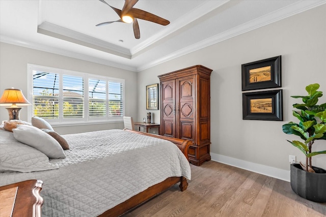 bedroom with light wood-type flooring, baseboards, a raised ceiling, and crown molding