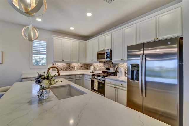 kitchen featuring light stone counters, a sink, white cabinetry, hanging light fixtures, and appliances with stainless steel finishes