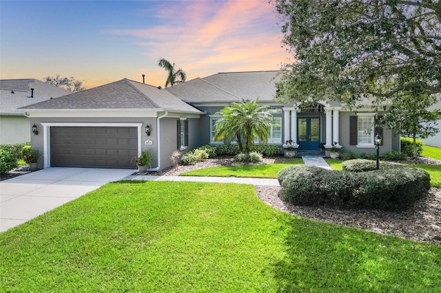 view of front of home featuring french doors, a yard, stucco siding, a garage, and driveway