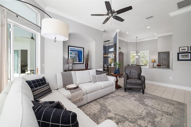 living area with visible vents, ornamental molding, tile patterned flooring, baseboards, and ceiling fan with notable chandelier