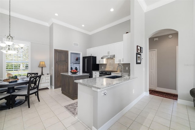 kitchen featuring arched walkways, washer and clothes dryer, a high ceiling, high end black refrigerator, and a sink