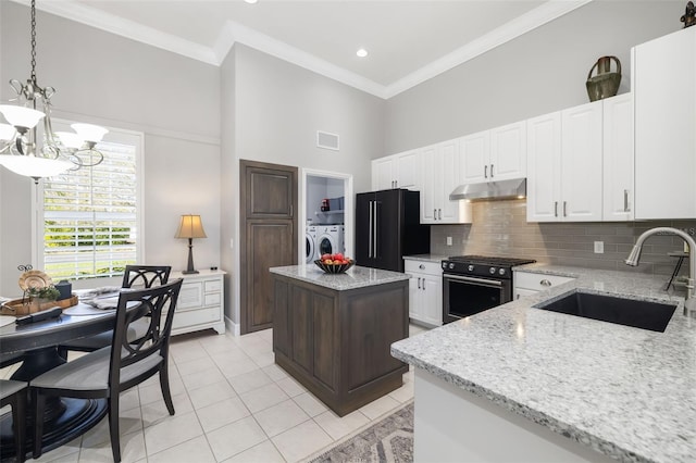 kitchen featuring washing machine and clothes dryer, freestanding refrigerator, gas range oven, under cabinet range hood, and a sink