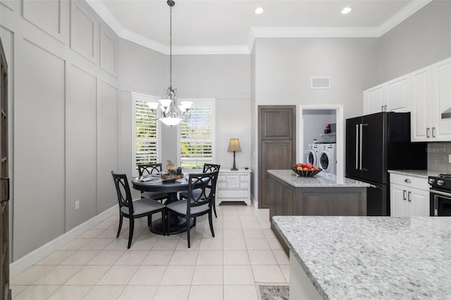 kitchen with crown molding, washing machine and clothes dryer, light tile patterned floors, freestanding refrigerator, and white cabinetry