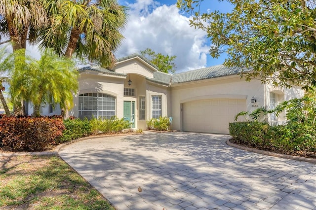 mediterranean / spanish-style home featuring a garage, decorative driveway, a tiled roof, and stucco siding