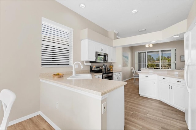 kitchen with light wood finished floors, appliances with stainless steel finishes, white cabinets, a sink, and a peninsula