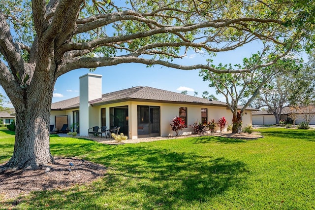 rear view of property featuring a chimney, an attached garage, a lawn, and stucco siding