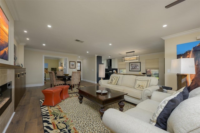 living area featuring a tile fireplace, recessed lighting, visible vents, dark wood-style floors, and crown molding