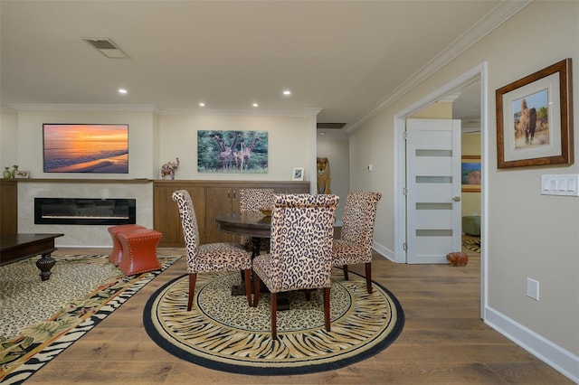 dining area with a fireplace, visible vents, dark wood-type flooring, ornamental molding, and baseboards