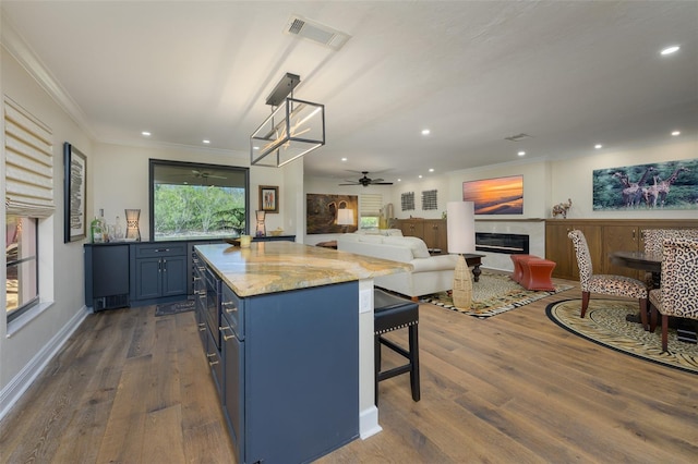 kitchen featuring visible vents, a glass covered fireplace, a kitchen breakfast bar, dark wood-style flooring, and blue cabinets