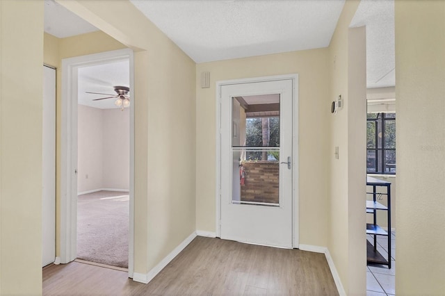 interior space featuring a ceiling fan, baseboards, light wood-style flooring, and a textured ceiling