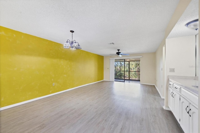 interior space with visible vents, a textured ceiling, light wood-type flooring, baseboards, and ceiling fan with notable chandelier