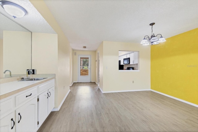 interior space featuring light countertops, white cabinetry, black microwave, pendant lighting, and a sink