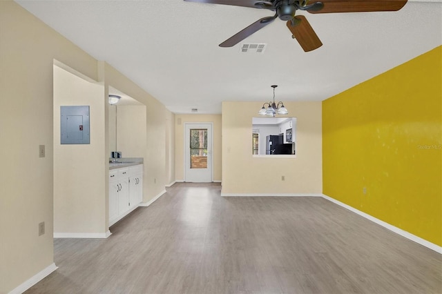 unfurnished living room featuring light wood finished floors, visible vents, electric panel, baseboards, and ceiling fan with notable chandelier